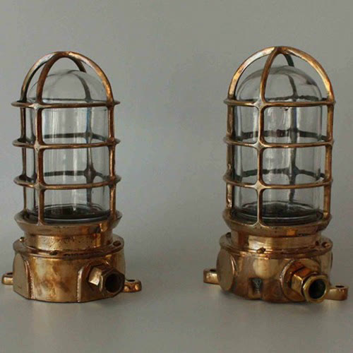 Authentic Pauluhn brass bulkhead wall lights with clear glass domes and protective cages, rewired with UL-listed parts for nautical and industrial interiors.