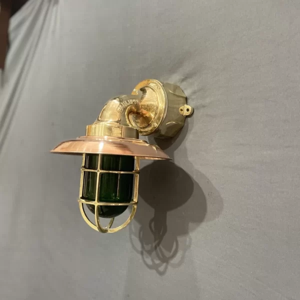 Brass and copper nautical wall sconce with green glass cage light. Vintage ship bulkhead light with green lens and brass cage. Handmade maritime wall lamp in brass and copper with green glass shade. Industrial coastal wall sconce with cage-protected green glass bulb cover.